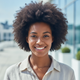 Close-up portrait of a smiling young Black woman, mid-20s, looking at the camera with a warm, trustworthy expression. She wea