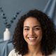 Portrait of a smiling young woman with a warm, trustworthy expression against a soft blue background.